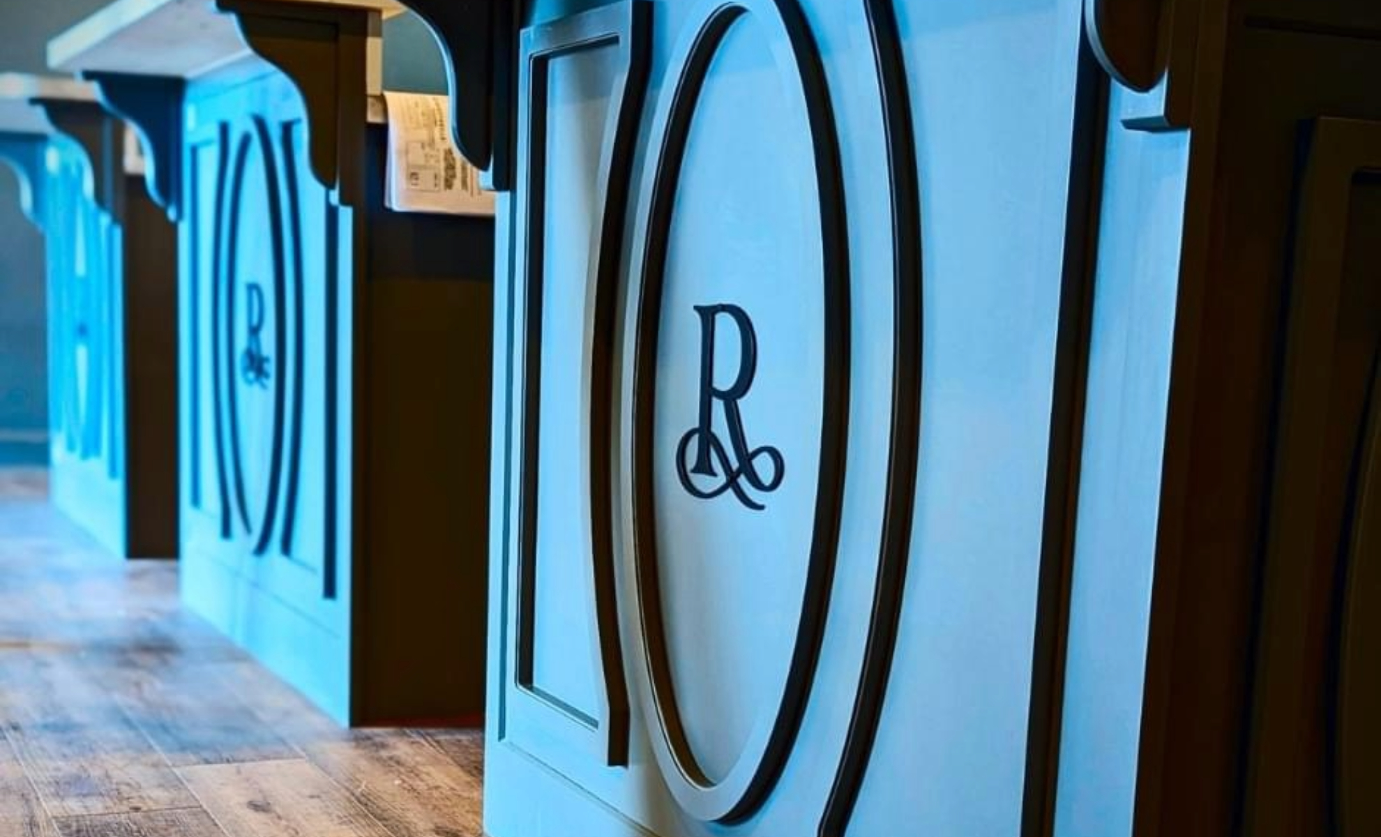 - The Renaissance Day Spa & Alternative Wellness, Fayetteville NC Close-up of decorative wooden panels with a large letter "R" in the center, installed along the base of a counter in a well-lit interior space. - The Renaissance Day Spa & Alternative Wellness, Fayetteville NC